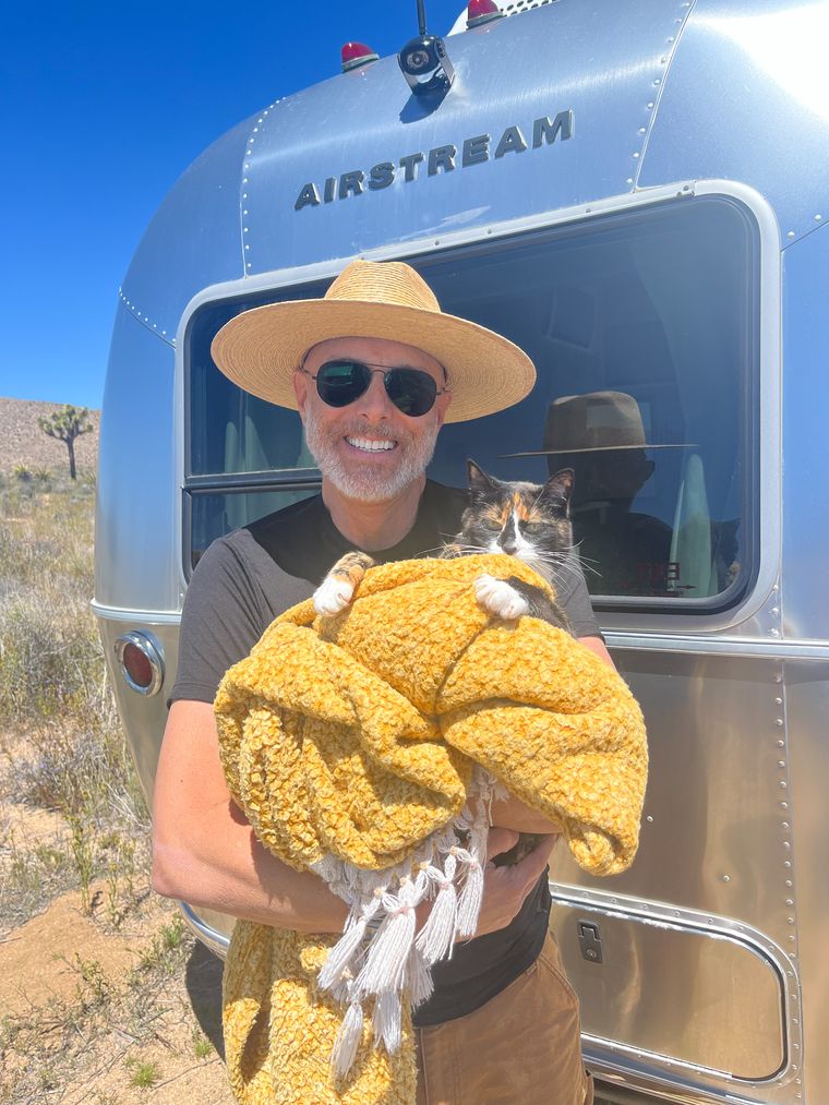 Holding a calico cat wrapped in a yellow blanket in front of an Airstream in the desert